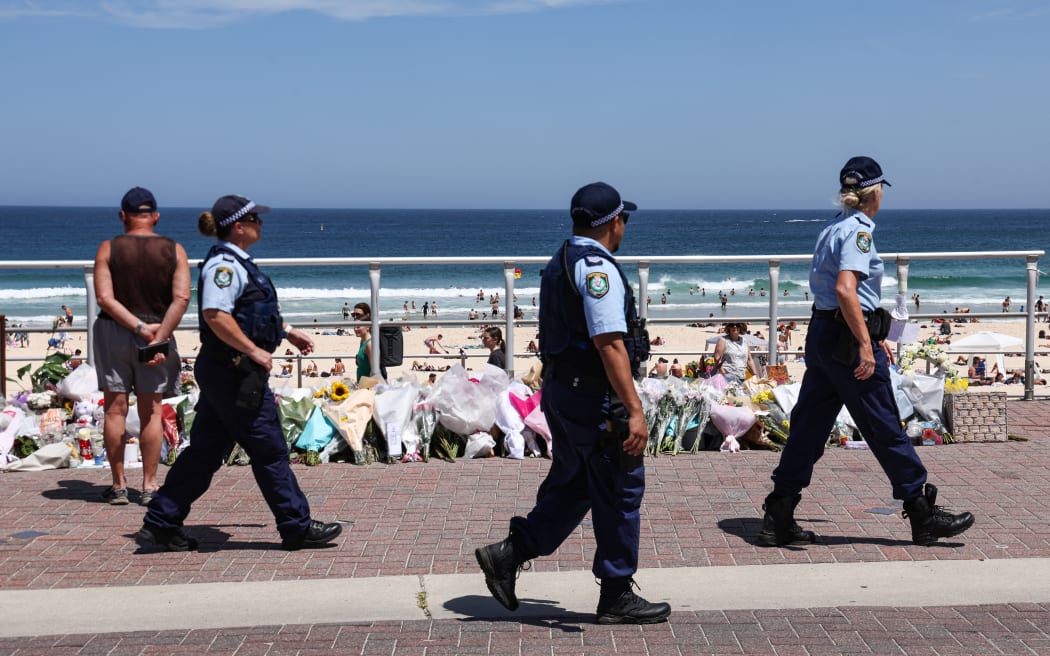 The Police walk past floral tributes left at the promenade of Bondi Beach in Sydney on 18 December, 2025, to honour victims of the shooting that took place there on 14 December.
