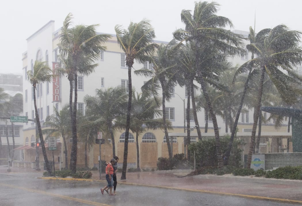 People walk down a Miami Beach  street as winds and rain from Hurridane Irma begin to hit.