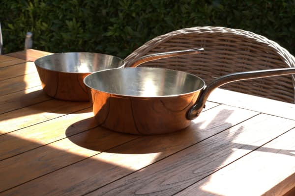 Stainless steel pans on wooden table in sunlight.