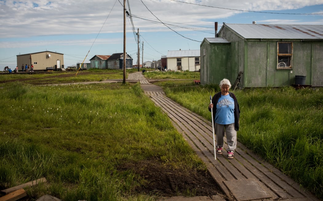 NEWTOK, AK - JULY 03: Mary Tom walks down a wooden sidewalk on July 3, 2015 in Newtok, Alaska. Newtok is one of several remote Alaskan villages that is being forced to relocate due to warming tempertures which is causing the melting of permafrost, widening of rivers and the erosion of land and coastline.   Andrew Burton/Getty Images/AFP (Photo by Andrew Burton / GETTY IMAGES NORTH AMERICA / Getty Images via AFP)