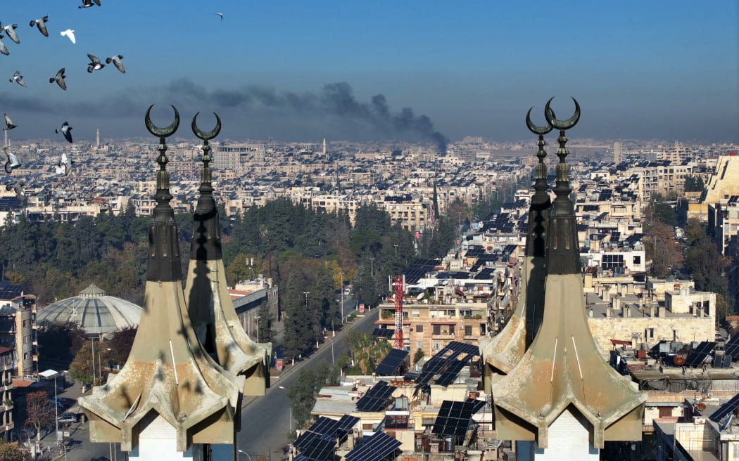 This aerial picture shows a partial view of Aleppo with smoke rising in the background after jihadists and their allies entered the northern Syrian city  on November 30, 2024. - Jihadists and their Turkish-backed allies breached Syria's second city of Aleppo on November 29, as they pressed a lightning offensive against forces of the Iranian- and Russian-backed government. (Photo by Omar HAJ KADOUR / AFP)