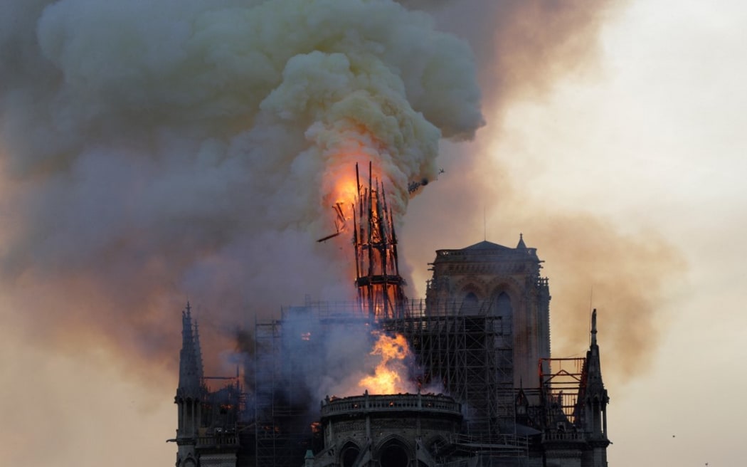 The steeple and spire engulfed in flames collapses as the roof of the Notre-Dame de Paris Cathedral burns on April 15, 2019 in Paris. - A colossal fire swept through the famed Notre-Dame Cathedral in central Paris on April 15, 2019, causing a spire to collapse and raising fears over the future of the nearly millenium old building and its precious artworks. The fire, which began in the early evening, sent flames and huge clouds of grey smoke billowing into the Paris sky as stunned Parisians and tourists watched on in sheer horror. (Photo by Geoffroy VAN DER HASSELT / AFP)