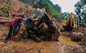 Rescue workers push a overturned vehicle stuck in the mud and debris at a site of a landslide  caused by heavy rains in Kokkayar in India's Kerala state on October 17, 2021.