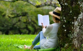 Woman sitting under a tree reading a book in the park