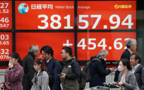 Pedestrians walk past an electronic board showing the closing numbers of the Tokyo Stock Exchange along a street in Tokyo on February 15, 2024.