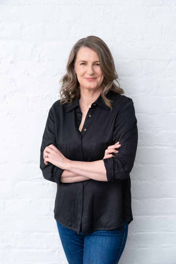Charlotte Purdy, in a black shirt, stands against a while wall with her arms folded.