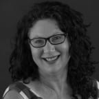 A black and white portrait of playwright Jane Harrison smiling at the camera.