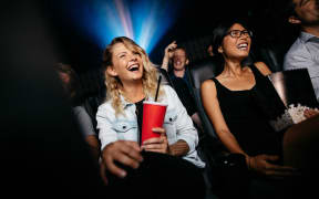 Young people laughing while watching film in movie theater.