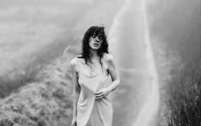 Susan walks down a misty country road wearing a slip dress, hair covering her face.