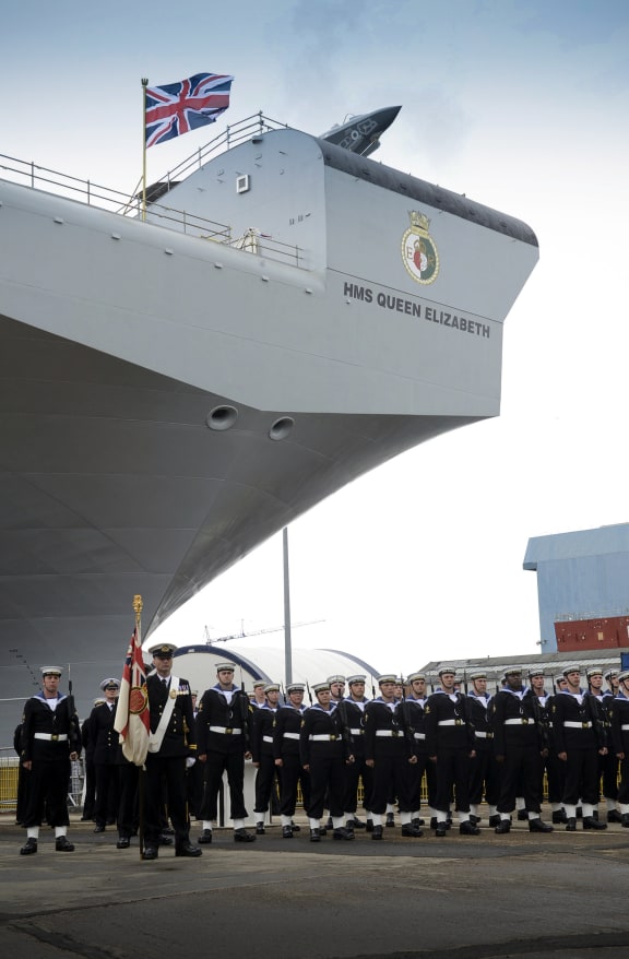 British Navy personnel stand to attention as Queen Elizabeth II smashes a bottle of whisky on the new aircraft carrier's bow.
