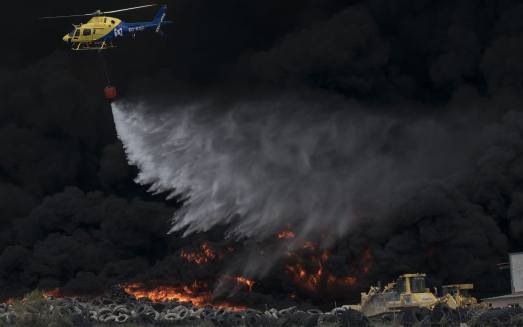 A helicopter drops water over tyres burning in an uncontrolled dump near the town of Sesena, Spain.