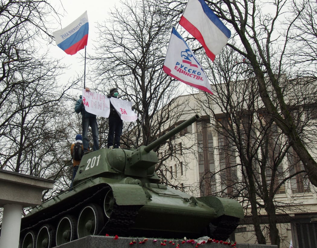 Pro-Russian demonstrators hold placards reading "Crimea for peace" as they stand on a T-34 Soviet tank, set as a WWII monument in front of the Crimean parliament in Simferopol  on February 27, 2014.