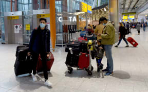 LONDON, ENGLAND - DECEMBER 21: Travellers wearing face coverings with their luggage in the almost deserted departures hall at Terminal 5 of Heathrow Airport in west London on December 21, 2020,