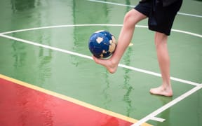 Barefoot boy playing football on a wet sports court.
