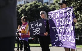 Bowel cancer protestors hold signs outside Parliament