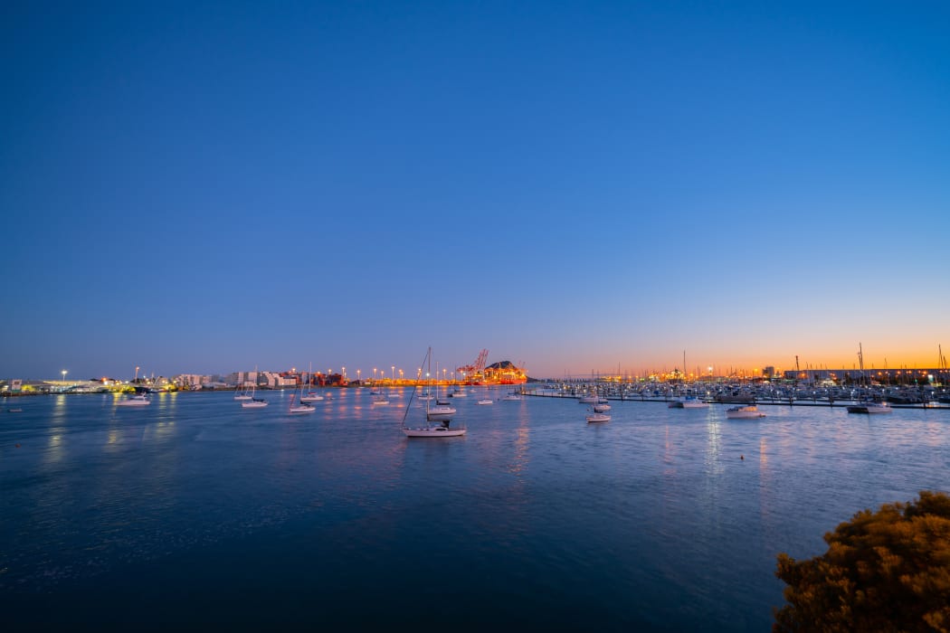 lights of Port of Tauranga ships and harbor at dawn with golden glow of sun on horizon.
