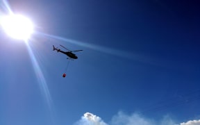 A helicopter with a monsoon bucket heads out to tackle the fire.