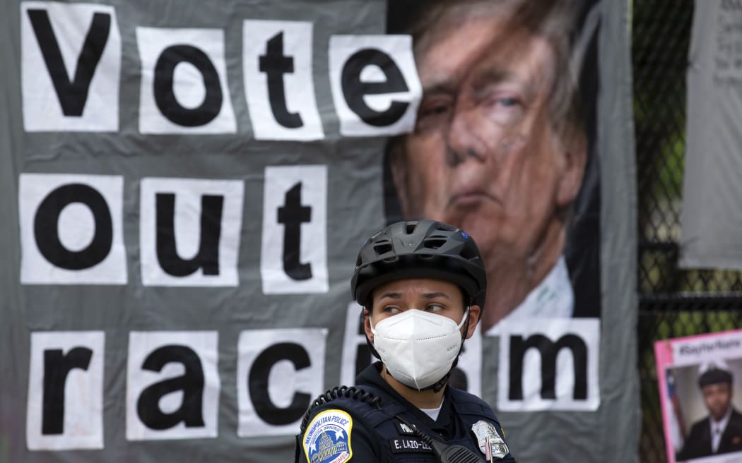 A Washington Police officer watches demonstrators march past Lafayette Square, near the White House ahead of the Fourth of July celebration on July 4, 2020, in Washington, DC.