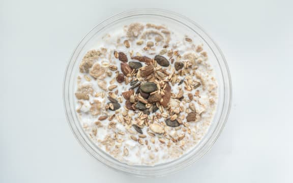 Bowl of oat porridge topped with seeds on a white table.