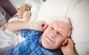 Senior man covers ears while wife snores