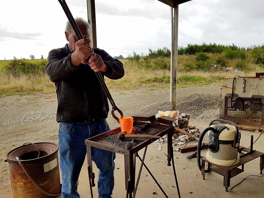 Allan Birchfield uses long tongs to handle the red hot crucible with molten gold inside; this is poured into a mould, plunged into water then tapped out.