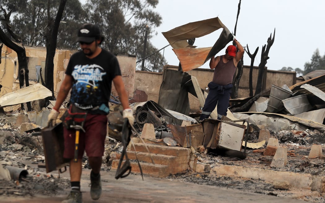 Men remove debris from houses destroyed by a forest fire in the hills of Tome, Concepcion province, Biobio region, Chile on February 4, 2023. - Chile has declared a state of disaster in several central-southern regions after a devastating heat wave provoked forest fires that left four people dead, authorities said on Friday. (Photo by JAVIER TORRES / AFP)