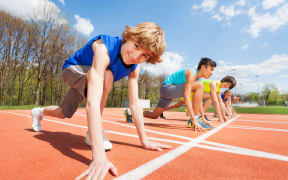 A photo of teenage athletes preparing to start running on the track on the stadium, side view