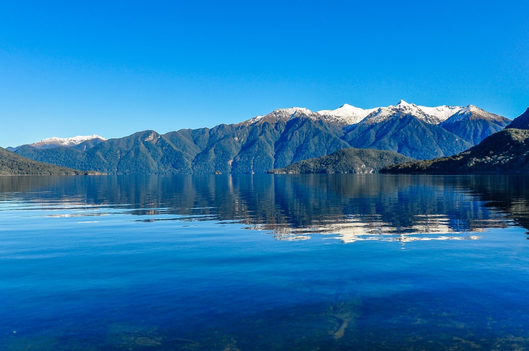 Reflection of snowy mountains in Lake Hauroko in the Southern Scenic Route, New Zealand