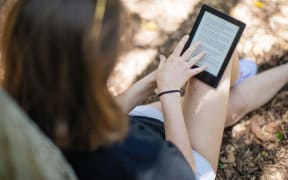 A woman reads an e-book in the shade under a tree