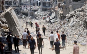 Palestinians make their way over the dirty of rubble, past destroyed buildings after the Israeli military withdrew following a two-week offensive from the Shujaiya neighbourhood, east of Gaza City on July 11, 2024, amid the ongoing conflict between Israel and the militant Hamas group. The civil defence agency in Hamas-run Gaza said on July 11, that around 60 bodies have been found in Gaza City's Shujaiya district, devastated by a two-week Israeli offensive. Israel said Wednesday it had ended its operation against Hamas militants in the district. (Photo by Omar AL-QATTAA / AFP)