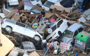 Persons climb on piled up cars following floods in Sedavi, south of Valencia, eastern Spain, on October 30, 2024. - Floods triggered by torrential rains in Spain's eastern Valencia region has left at least 70 people dead, rescue services said on October 30. (Photo by Jose Jordan / AFP)