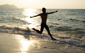 Silhouette of a man jumping on the beach at sunset.