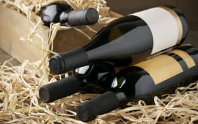 Assorted closed wine bottles lying on straw and vintage wooden box.