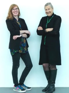 Two women wearing black clothes smile at the camera.