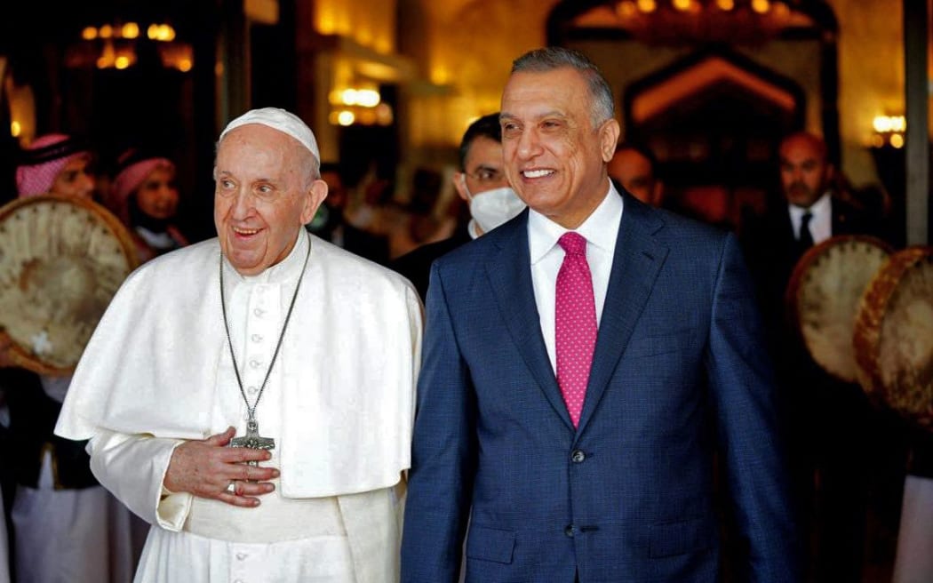 A handout image released by the press office of Iraqi Prime Minister on its Facebook page on March 5, 2021 shows Prime Minister Mustafa al-Kadhemi receiving Pope Francis upon his arrival in the capital Baghdad.