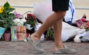 A man pauses at floral tributes on Bondi Beach to pay his respects to the victims of the Sydney shooting, December 16, 2025. A father-and-son team toting long-barrelled guns shot and killed 15 people including a 10-year-old girl at Sydney's Bondi Beach on December 14, with authorities labelling it an antisemitic terrorist attack on a Jewish festival. (Photo by DAVID GRAY / AFP)