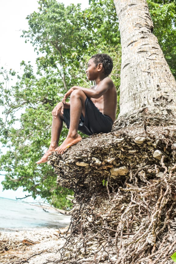 Joachim sitting under a coconut palm that is highly likely to be washed away before he is eight.