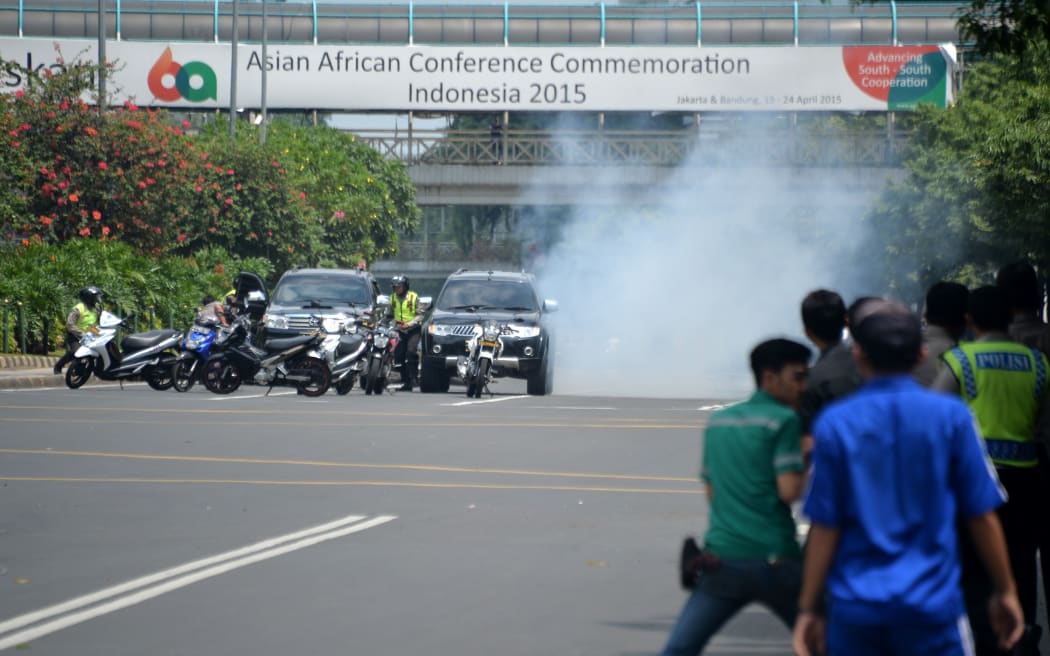 Police (L) hide behind vehicles during an exchange of gunfire with suspects hiding near a Starbucks cafe when another blast hits.