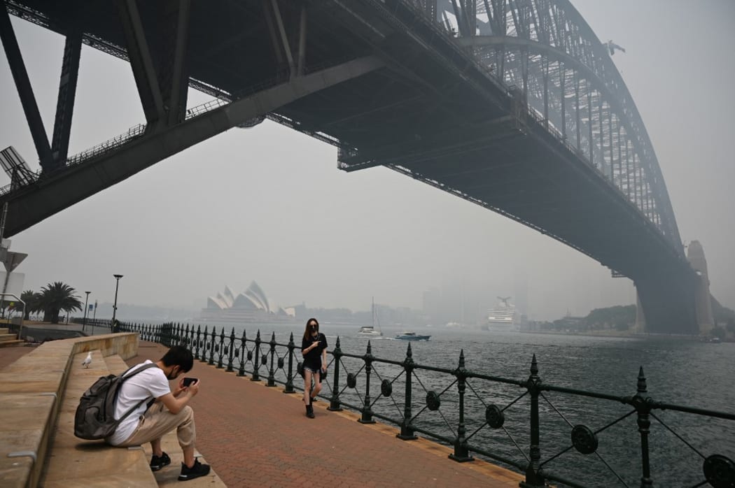 Tourists wearing masks take photos under the Harbour Bridge enveloped in haze caused by nearby bushfires, in Sydney on December 10, 2019.