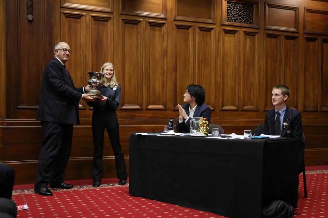 Wellington Black's Julia Randerson take the champions trophy from President Kos. Tony Huang and Benjamin Penno look on.