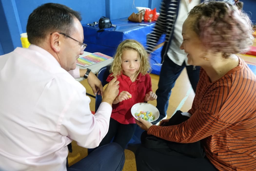 Whangarei National MP Shane Reti vaccinated 6 yr old Pippa Howie at Hikurangi School while mum Alysha looks on.