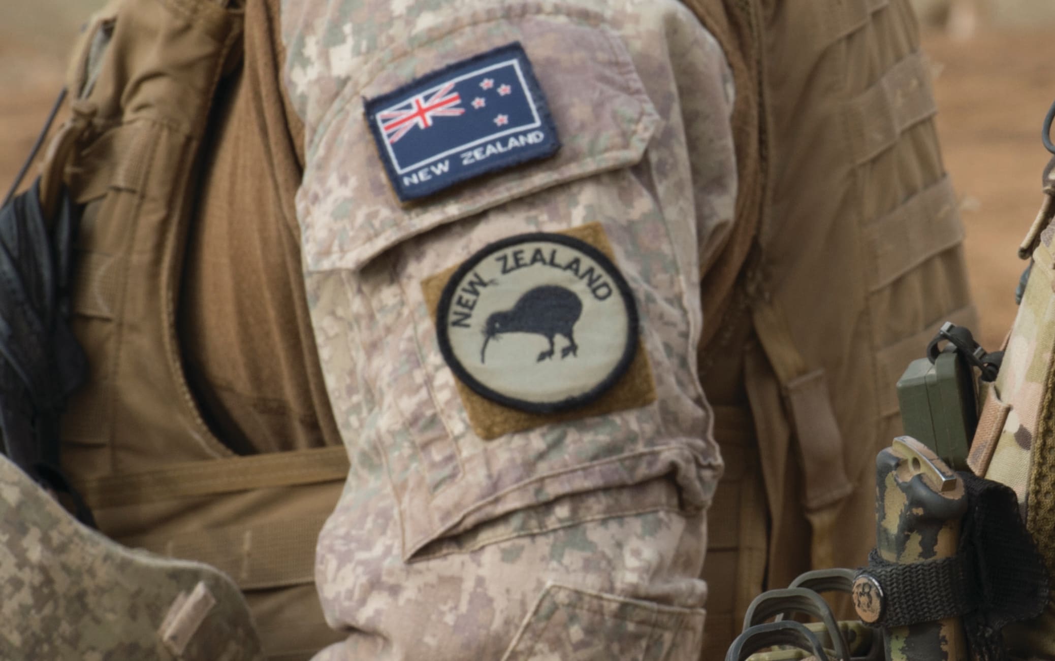 Close up of New Zealand and Australian soldiers side by side in uniform with their country flag on their sleeves.