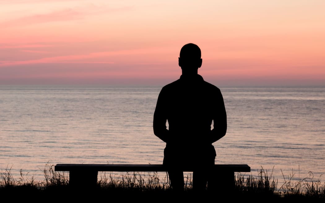 Silhouette of male person against a colorful horizon.