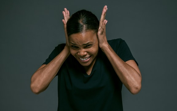 A woman in a black t-shirt covers her ears with her palms.
