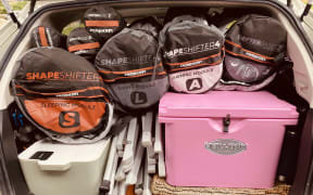 Duffle bags sit neatly on top of containers, tent poles and chilly bin in a car boot.