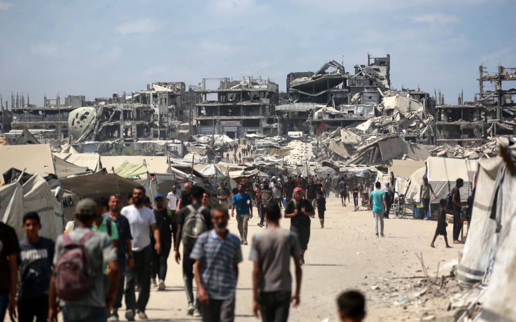 Palestinians walk along a street near war-damaged buildings in Gaza City on August 8, 2025. Israel's military will "take control" of Gaza City under a plan proposed by Prime Minister Benjamin Netanyahu and approved by his security cabinet, triggered a wave of criticism from across the world. (Photo by Bashar TALEB / AFP)