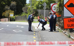 Lights are out at Birkenhead Ave intersection with Onewa Road and traffic is being manually directed by a person in a high-vis vest while armed police guard a cordon.