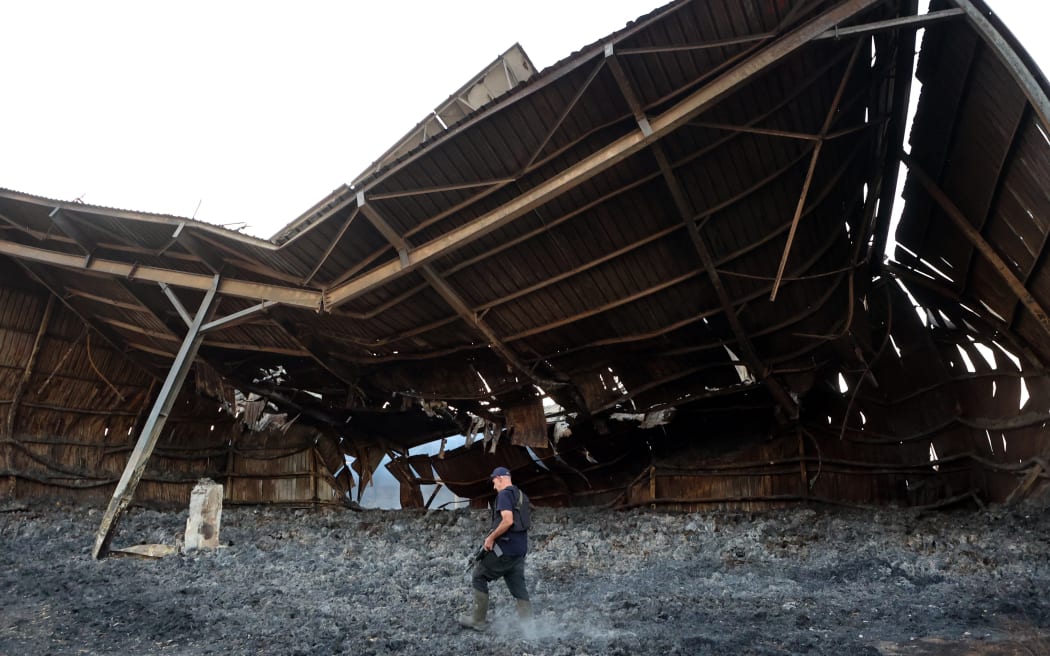 An armed resident walks amid the ashes of a heavily damaged building in kibbutz Alumim in southern Israel near the Gaza Strip on 18 October 2023. Thousands of people, both Israeli and Palestinians have died since October 7, 2023, after Palestinian Hamas militants based in the Gaza Strip, entered southern Israel in a surprise attack leading Israel to declare war on Hamas in Gaza on October 8. (Photo by GIL COHEN-MAGEN / AFP)