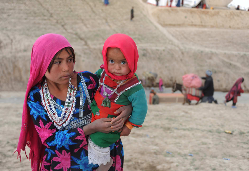 An Afghan girl holds her sister at landslide which turned 300 homes into a mass grave for over 2000 people.