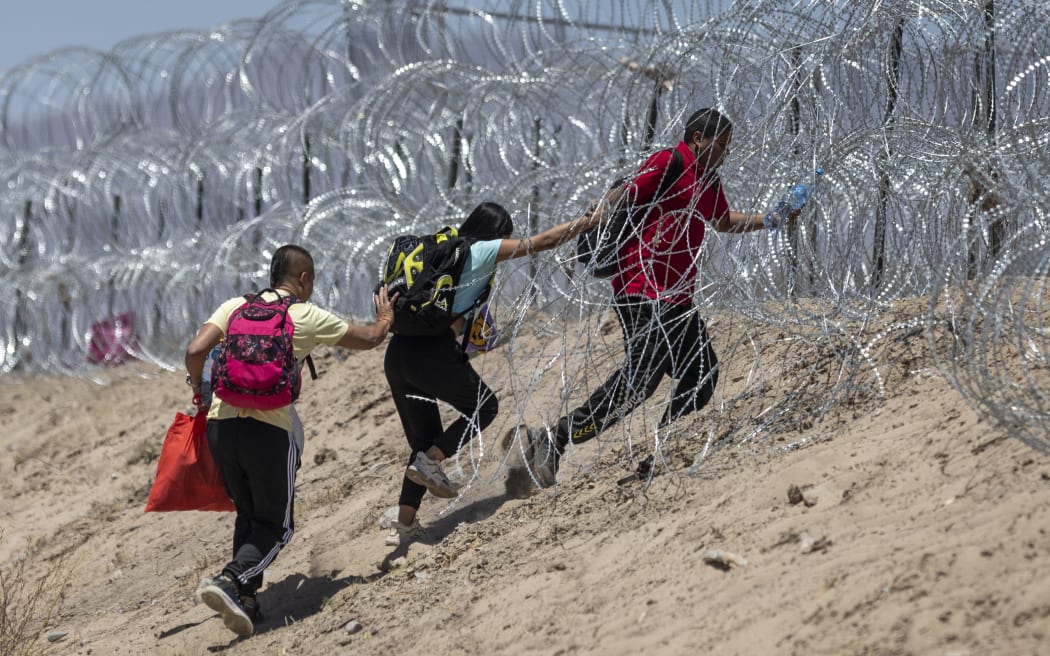 EL PASO, TEXAS - MAY 11: Immigrants walk through razor wire surrounding a makeshift migrant camp after crossing the border from Mexico on May 11, 2023 in El Paso, Texas. The number of immigrants reaching the border has surged with the end of the U.S. government's Covid-era Title 42 policy, which for the past three years has allowed for the quick expulsion of irregular migrants entering the country.   John Moore/Getty Images/AFP (Photo by JOHN MOORE / GETTY IMAGES NORTH AMERICA / Getty Images via AFP)